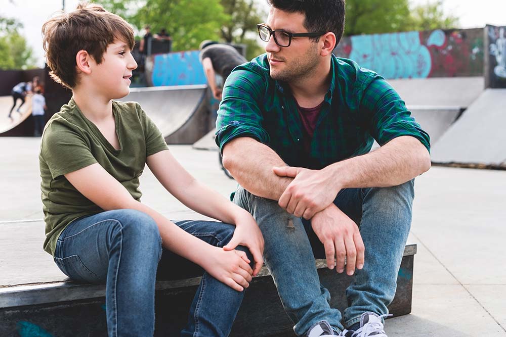 Male adult carer chatting casually to teen boy in Skate park
